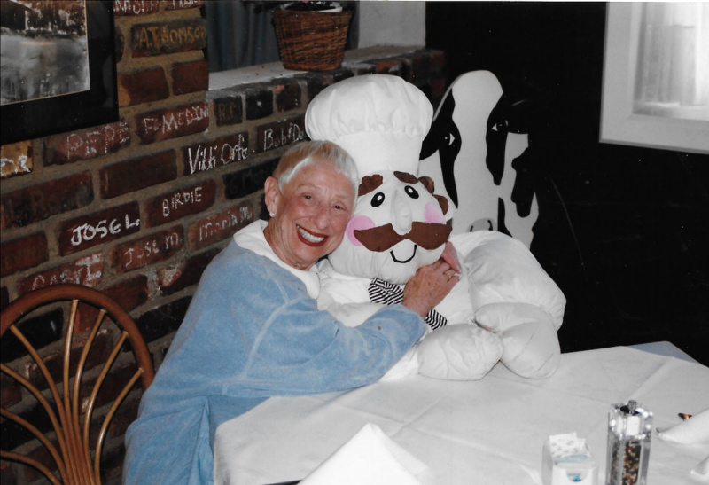   Steponas Spielbergas's mother Leah Adler sitting in a booth at her restaurant, The Milky Way, with her arms around a life-size stuffed chef.