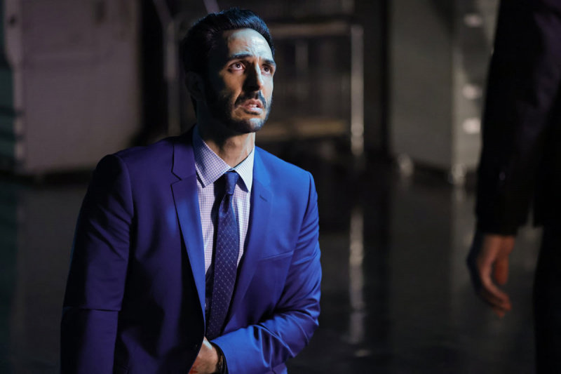   Amir Arison som Aram Mojtabai iført blå jakke og slips med venstre hånd under jakken i NBC-serien, The Blacklist