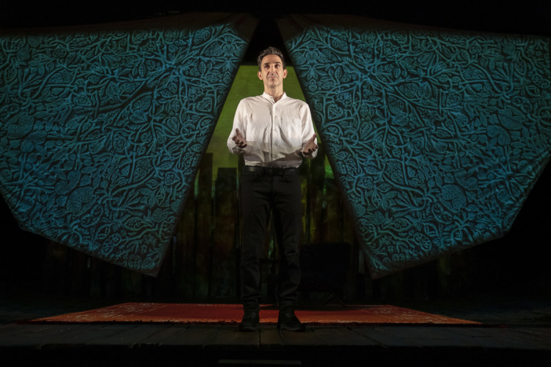   Amir Arison som Amir står i centrum. Hans ben er i skygge. Han har hænderne ud foran sig, bøjede albuer, håndfladerne opad, i The Kite Runner på Broadway's Hayes Theatre