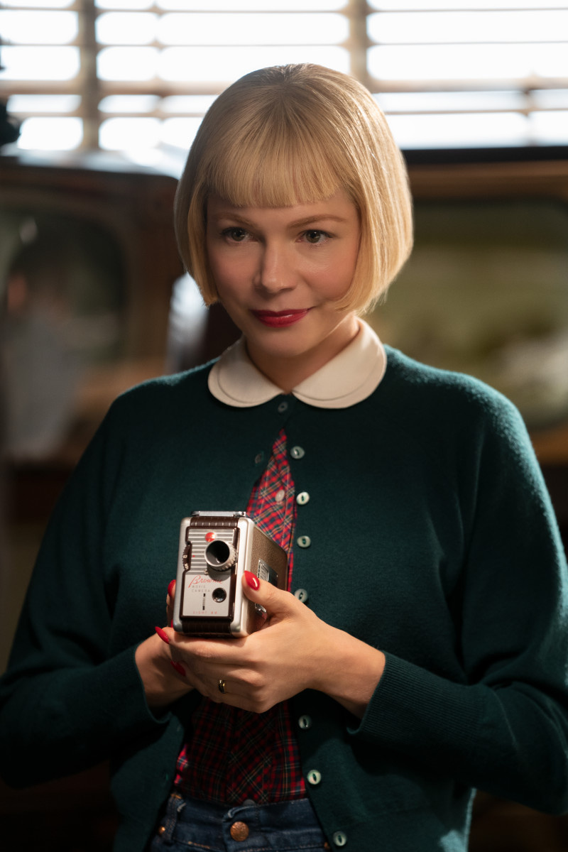   Michelle Williams nei panni di Mitzi Fabelman, che indossa una camicia a quadri rossa sotto un maglione verde, con in mano una macchina fotografica, nel film della Universal Pictures, The Fablemans