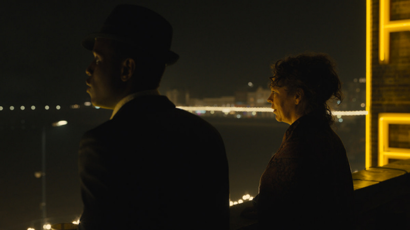   Michealas Wardas ir Olivia Colman naktį stovi ant stogo ir žiūri iš vandens telkinio „Searchlight Pictures“ filme „Šviesos imperija“