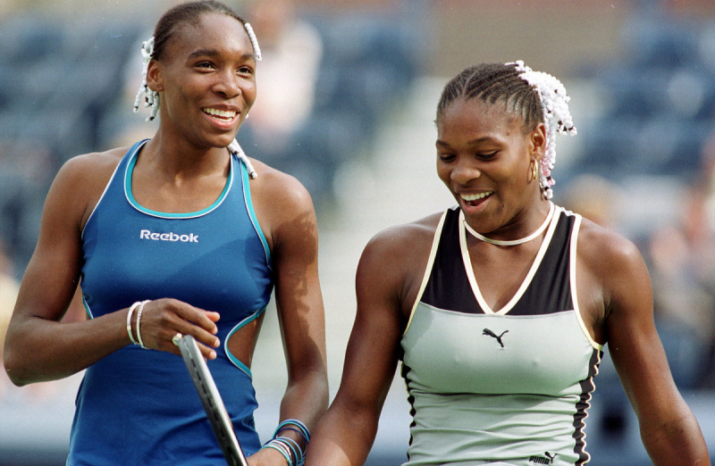   Venus Williams (L) ir jos sesuo Serena Williams dalijasi lengvu momentu per Moterį's Doubles match against Miho Saeki and Yuka Yoshida on Thursday September 2, 1999 at the 1999 US Open in New York. The Williams sisters won their match 6-2, 6-3.