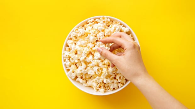  popcorn-sedda-från-ovan-på-gul-bakgrund-kvinna-äter-popcorn-mänsklig-hand-vy ovanifrån