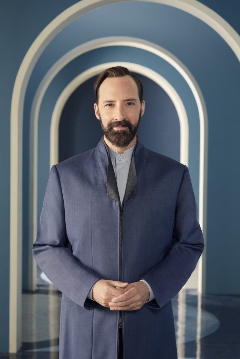 Tony Hale nei panni di Mr. Curtain indossa un abito grigio scuro e una maglietta grigio chiaro della serie Disney+, The Mysterious Benedict Society