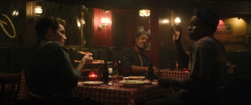   Rodney Burford als Tony Hughes sitzt mit zwei anderen Männern in einem Restaurant, isst Pizza und trinkt"DAHMER - Monster: The Jeffrey Dahmer Story" on Netflix