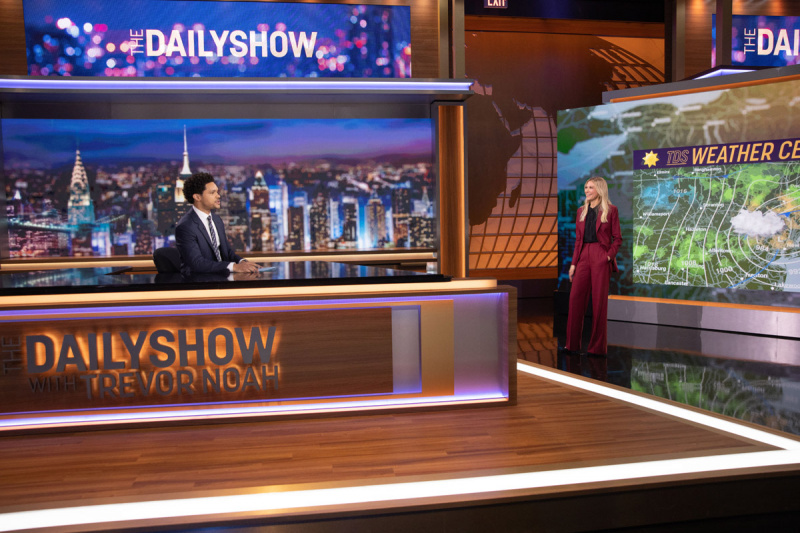   Desi Lydic staat voor een weerkaart en praat met Trevor Noah die aan zijn bureau zit op de set van The Daily Show op Comedy Central.