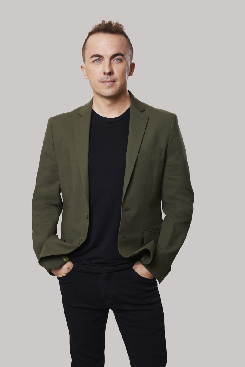   Frankie Muniz dėvi juodas kelnes ir marškinėlius su alyvuogių pilku VH1 švarku"The Surreal Life"