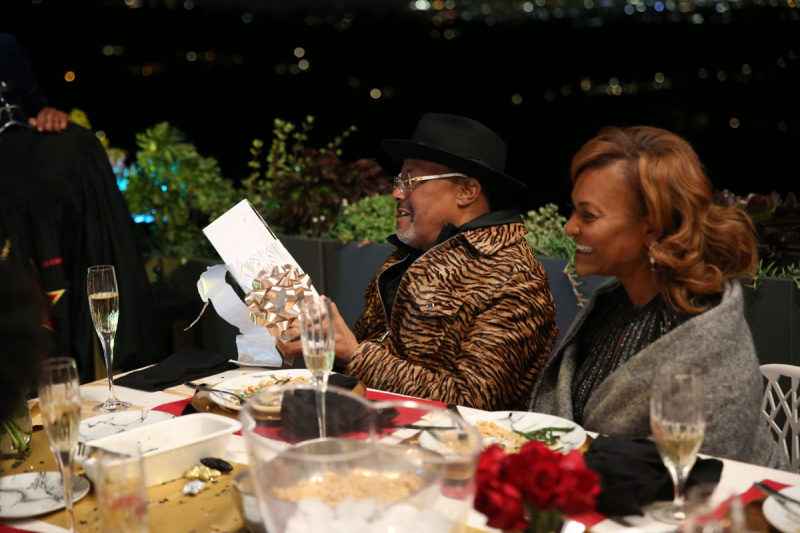   Rechter Greg Mathis in een jasje met tijgerprint en een hoed met brede rand, kijkend naar een menukaart aan een tafel met glazen champagne met vrouw, Linda in de E Entertainment Television-show, Mathis Family Matters.